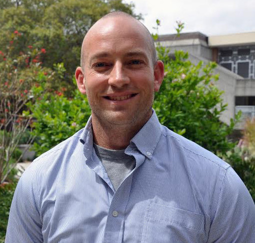 Photo of Jon Matheson on campus with greenery and building background